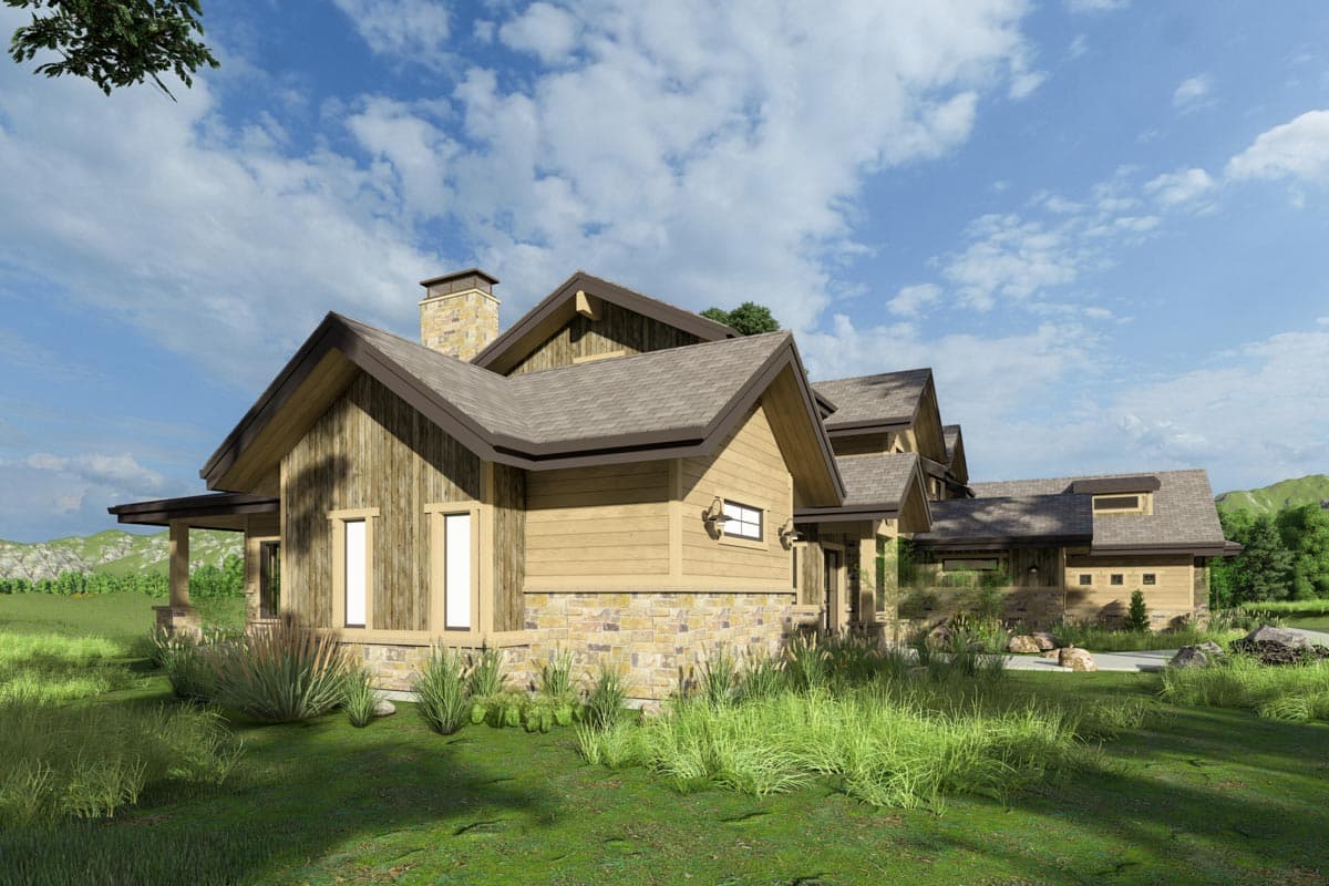 A modern, multi-gabled house with a stone chimney and siding. Lush green grass and a blue sky with clouds in the background.
