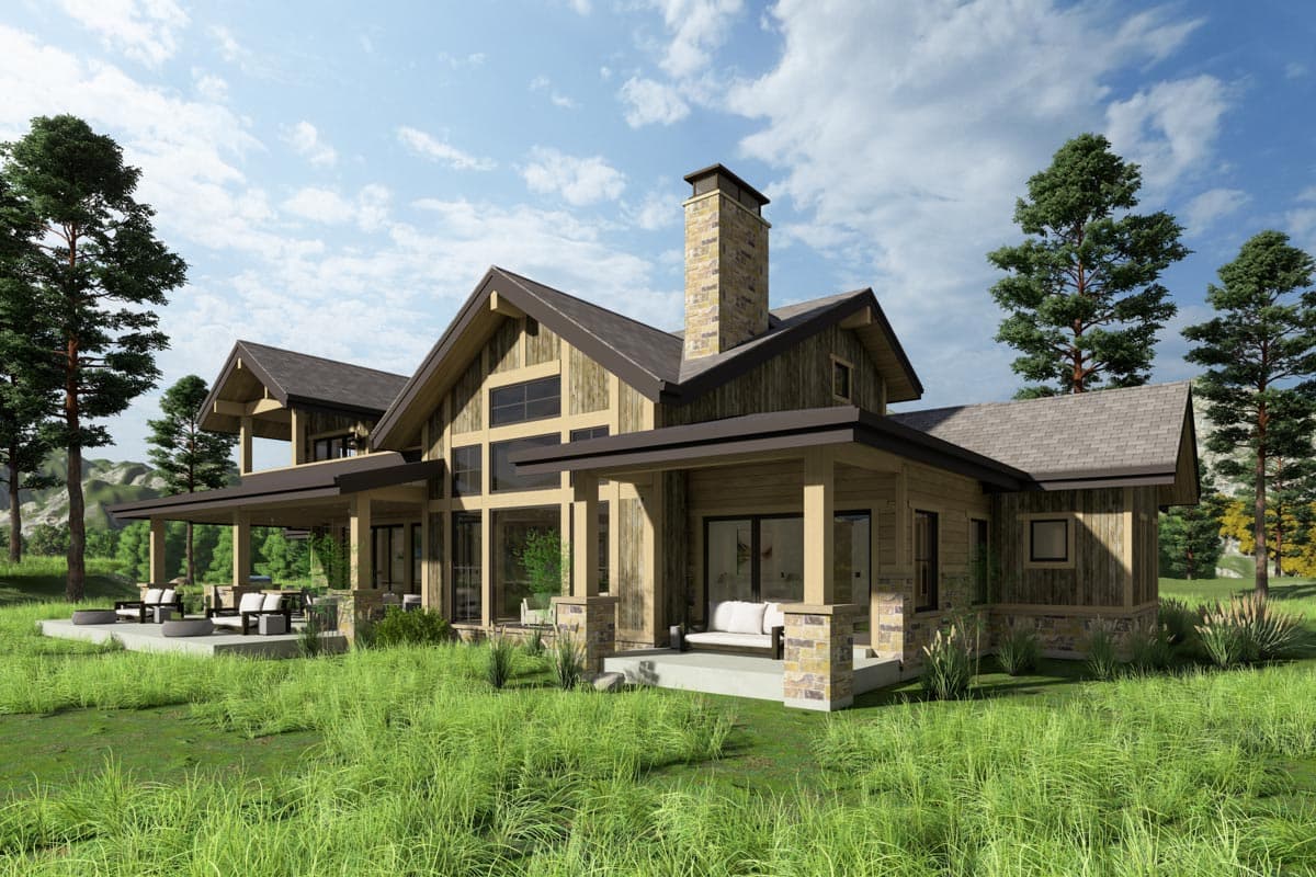 A rustic house with a large covered porch and stone chimney sits in a grassy area with trees and a cloudy sky in the background.