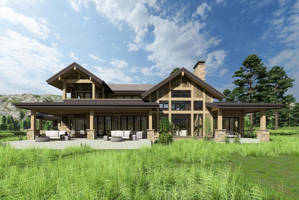 A large, modern wooden house with a spacious porch and large windows sits in front of a green field, under a bright, cloudy sky.