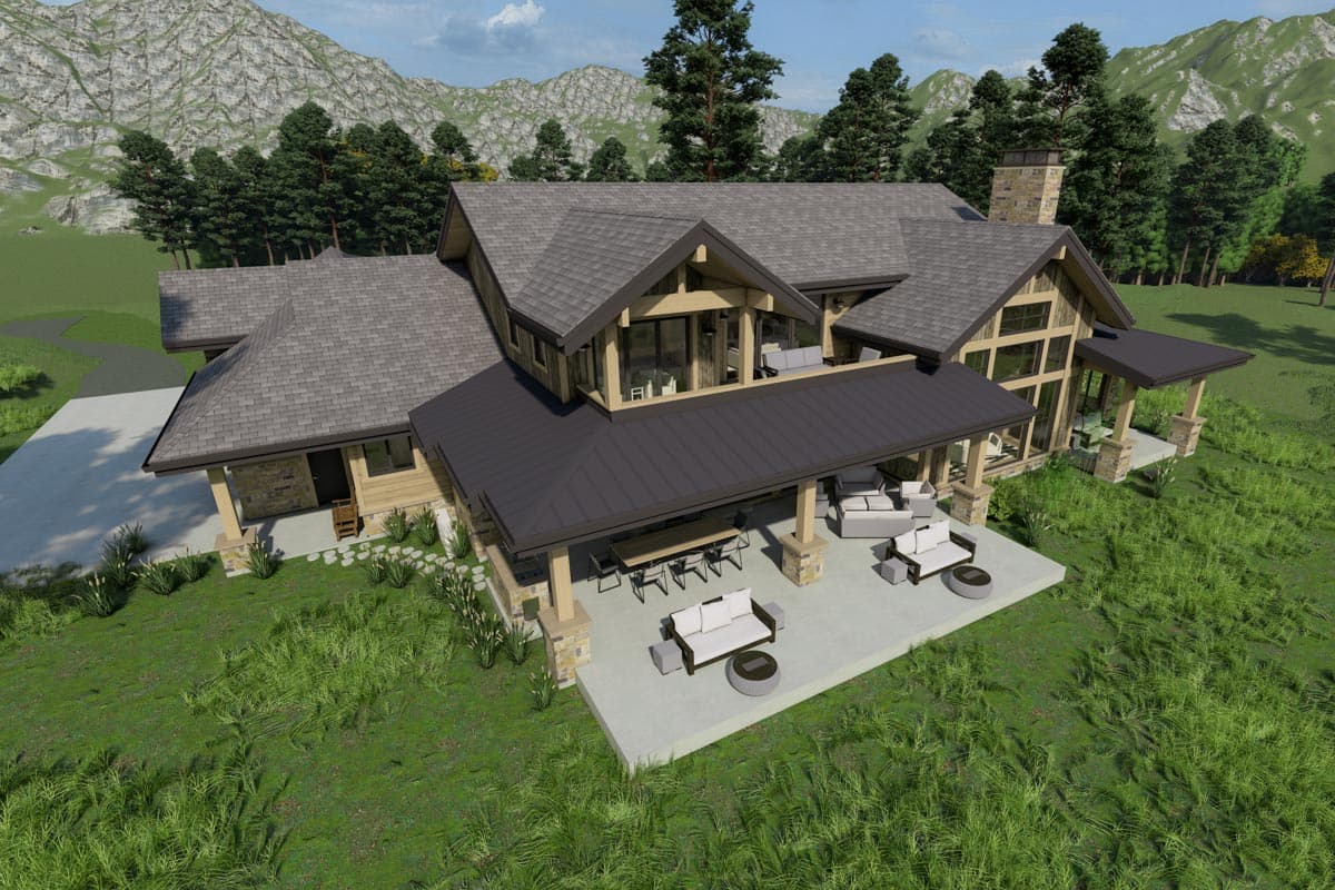 An aerial view of a large cabin-style house with a covered patio, outdoor seating, and a mountainous backdrop.