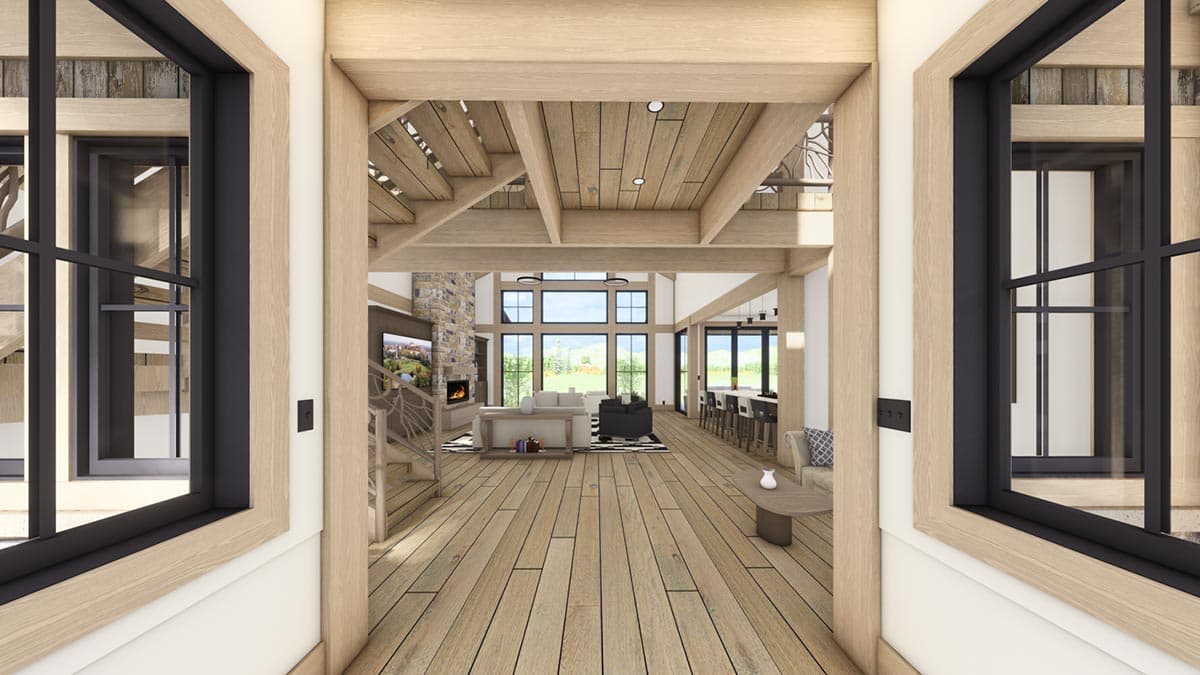 Interior view of a modern living area with wooden floors, tall windows, and a staircase. The entrance frames the view.