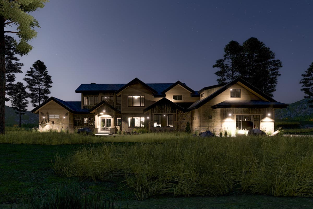 A large, multi-gabled house illuminated at night. Lights glow from windows and porch areas against a starlit sky, set among tall grasses.
