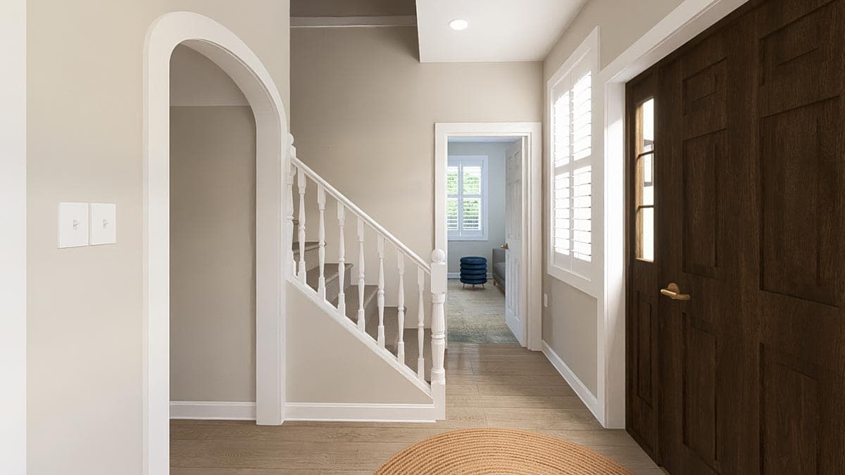 Entryway with arched doorway, white baluster staircase, dark wood door with sidelight, and interior view of a room with blue ottoman.