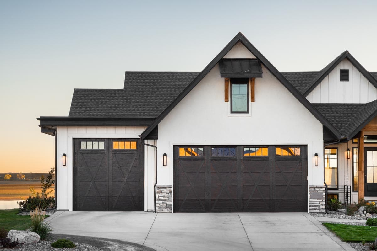 Modern Farmhouse house plan exterior with a white stucco finish, a large gable with black metal roof, and dark wood garage doors.