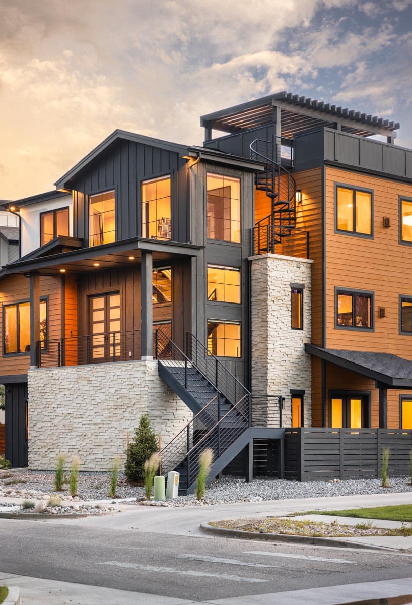 Contemporary house plan exterior with dark vertical siding, wood siding, stone base, and exterior spiral staircase.