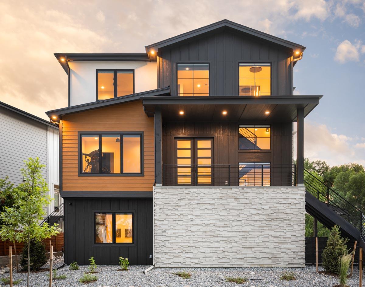 Modern house plan exterior with wood siding, dark paneling, and stacked stone base. Features a covered balcony and multiple gables.