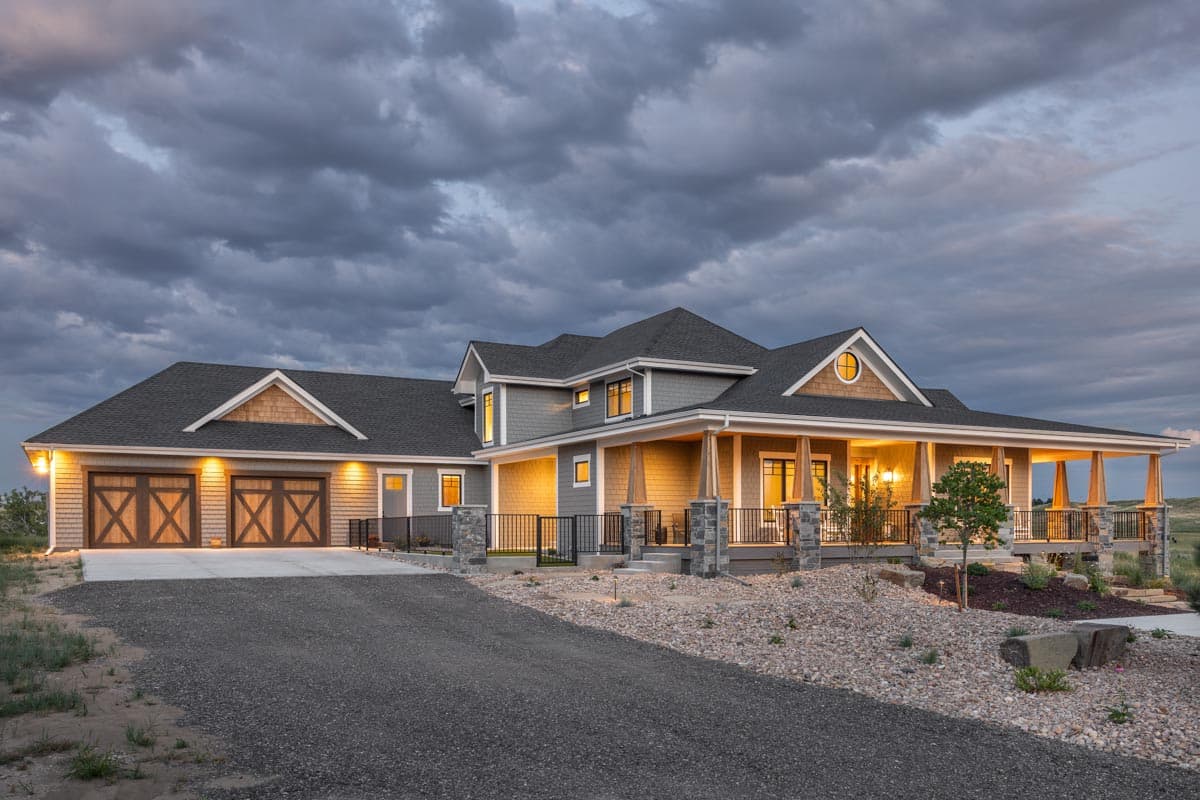 House plan exterior showing a two-story home with a wide wrap-around porch, gabled dormers, and a three-car garage.