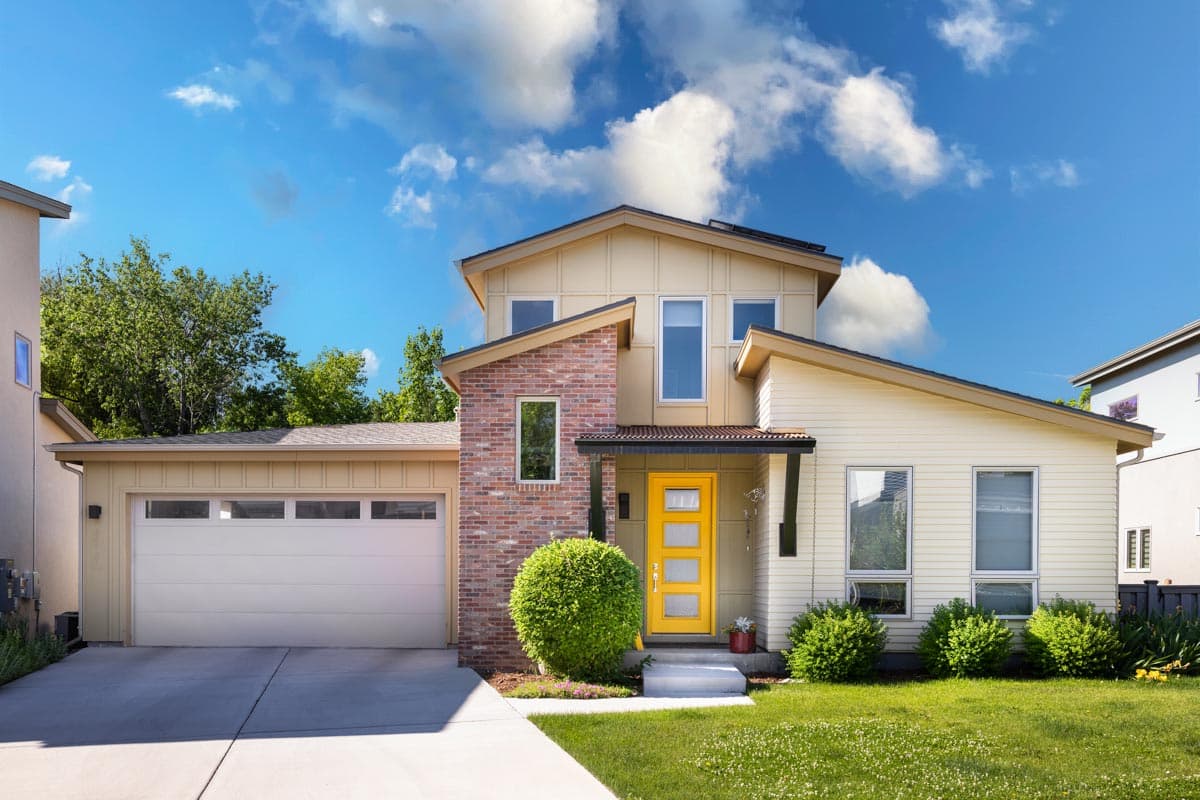 House plan exterior. Two-story Modern house with brick accent, shed roof, and attached garage. Includes a covered entry and a yellow front door.