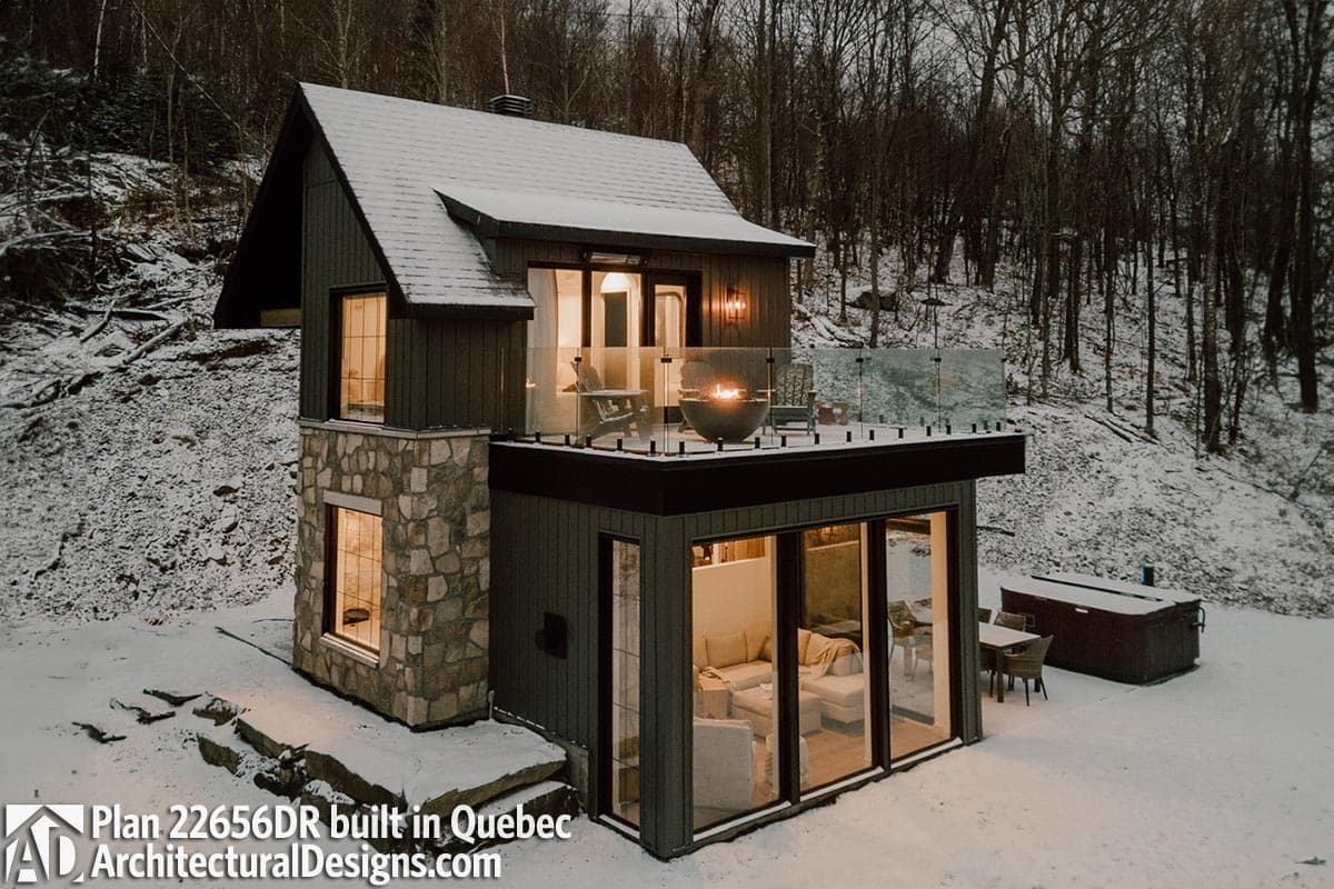 House plan exterior: two-story modern home with stone base, deck with glass railing, and large windows.