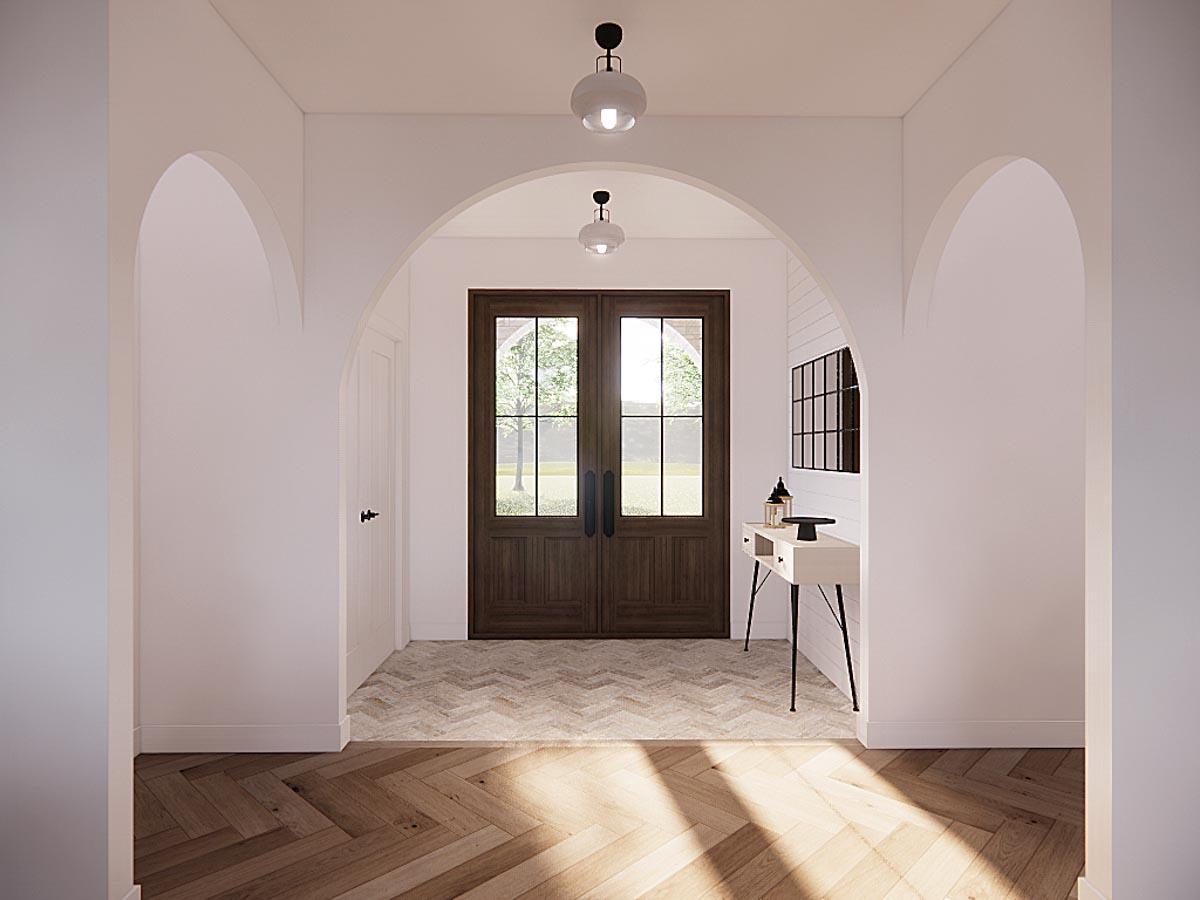 A hallway with arched doorways leads to a set of wooden doors. A console table with a decorative mirror and lighting fixtures sits on the right.