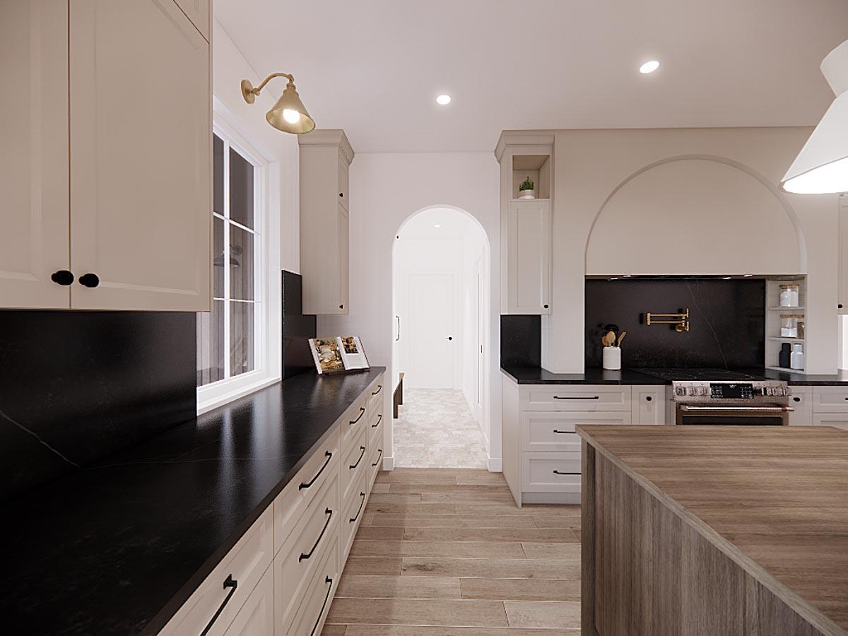 A modern kitchen with white cabinets, black countertops, and a wooden island. An archway leads to a hallway. Natural light streams in from a window.