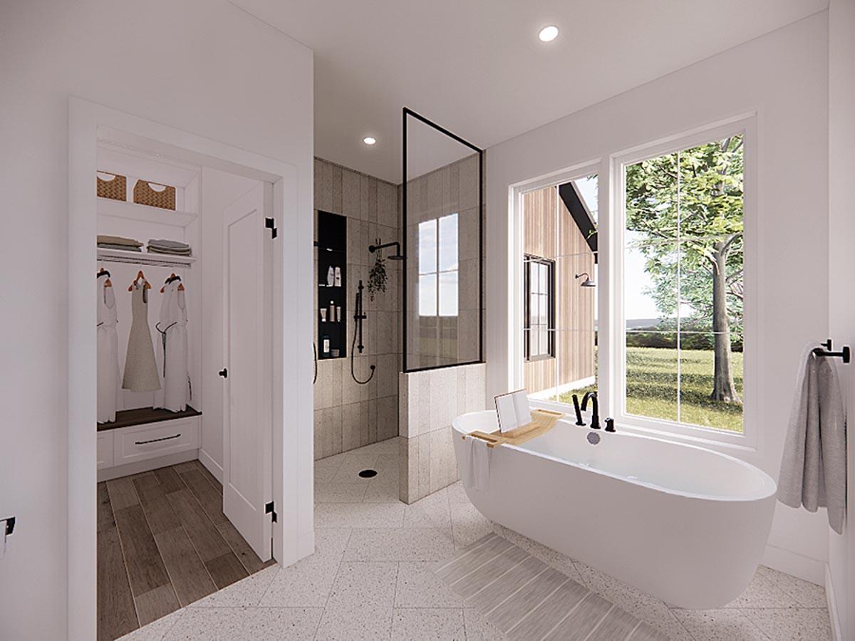 Modern bathroom with a freestanding tub near a large window overlooking a lush landscape. Shower and closet visible in the background.