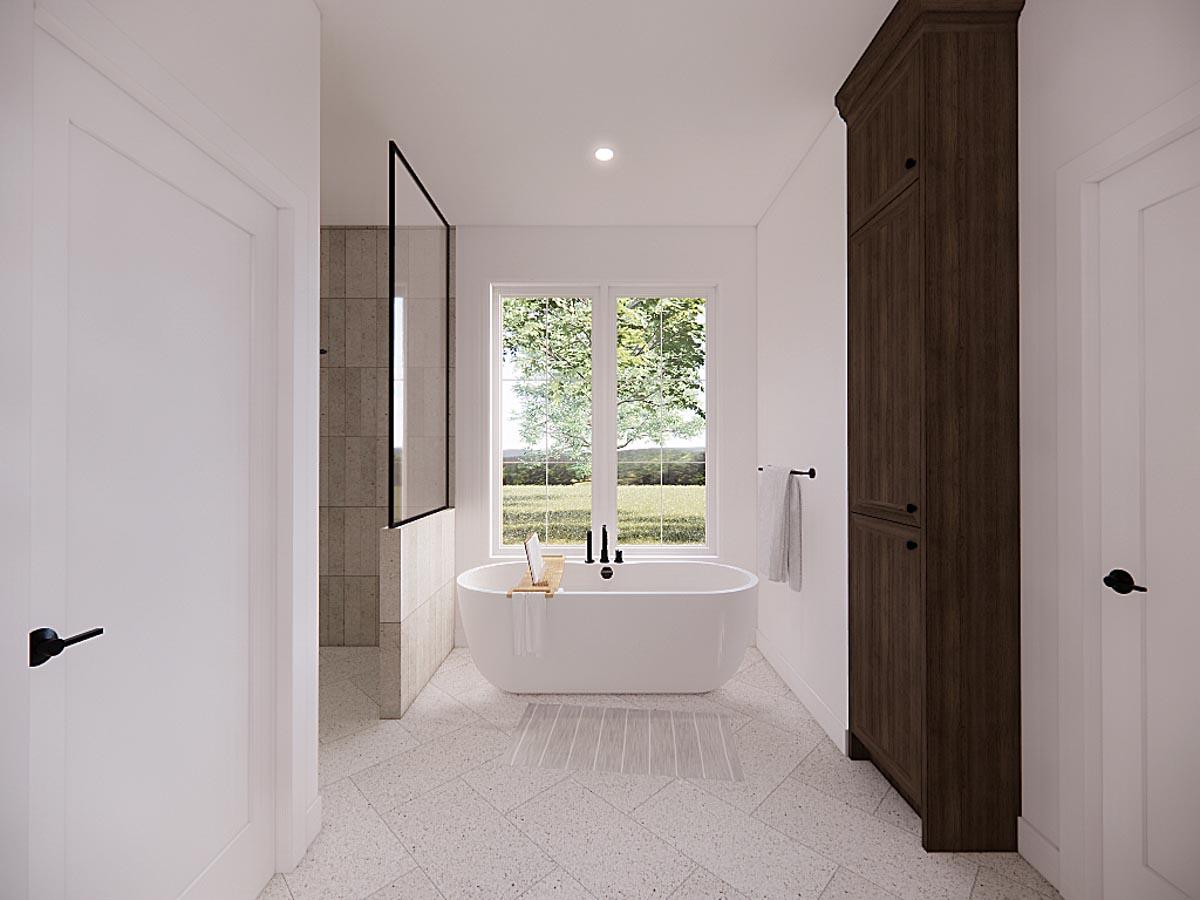 A modern, well-lit bathroom with a freestanding tub near a window overlooking a green landscape, with a dark wood storage cabinet nearby.