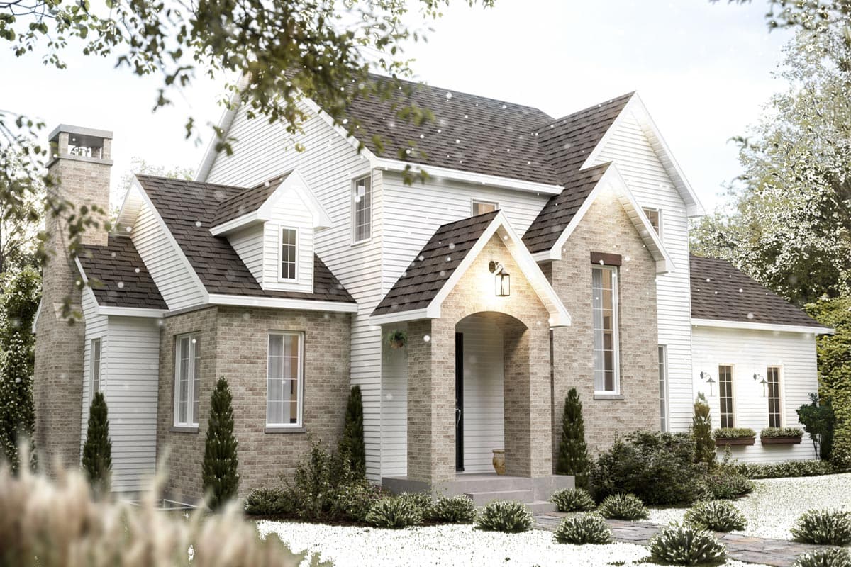 A two-story white house with brick accents, dormer windows, and a dark shingle roof, appears to be in a snowy landscape with bushes and evergreen trees.