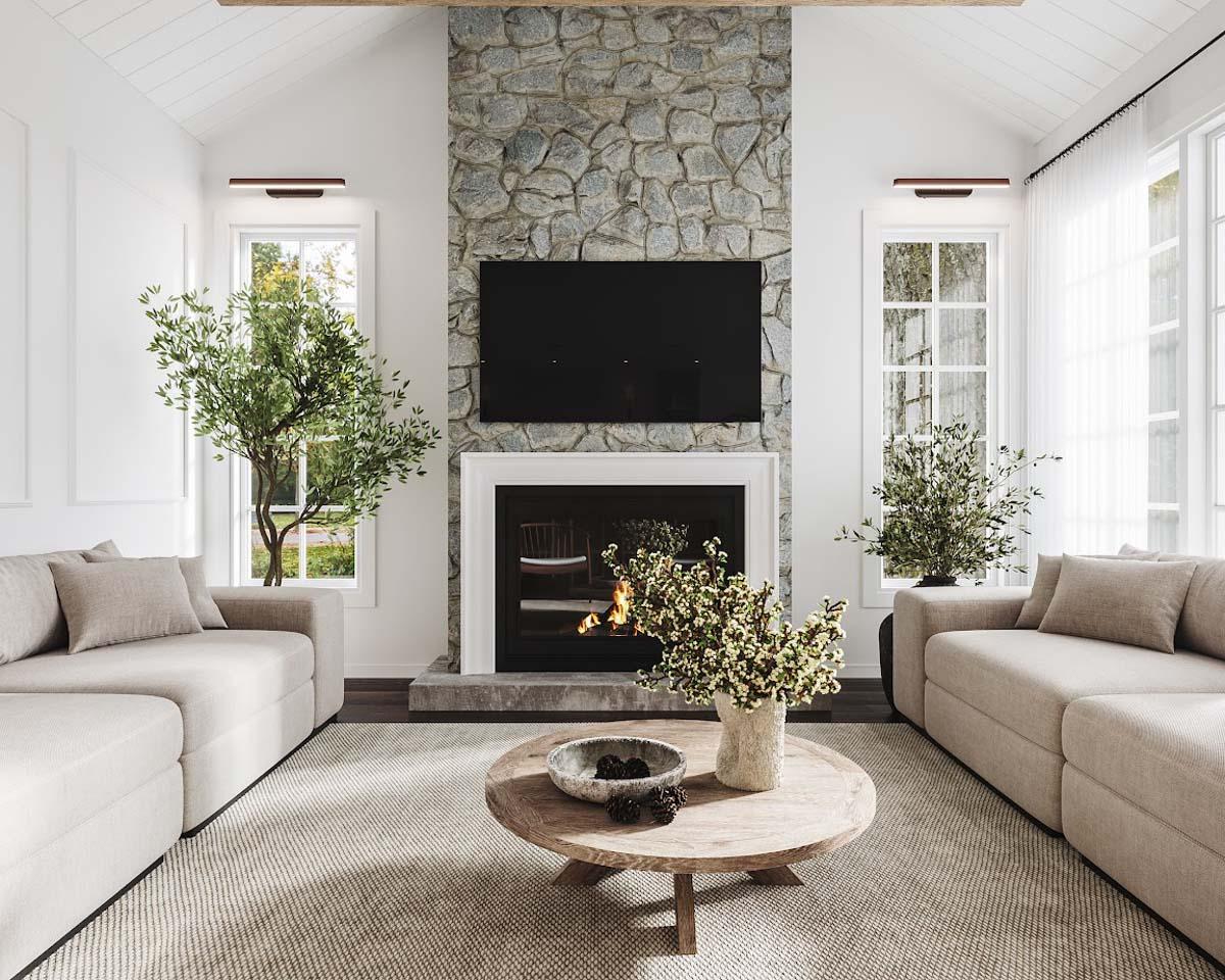 Cozy living room with a stone fireplace, large TV, and two beige sofas facing each other. A round coffee table sits in front of the fireplace.