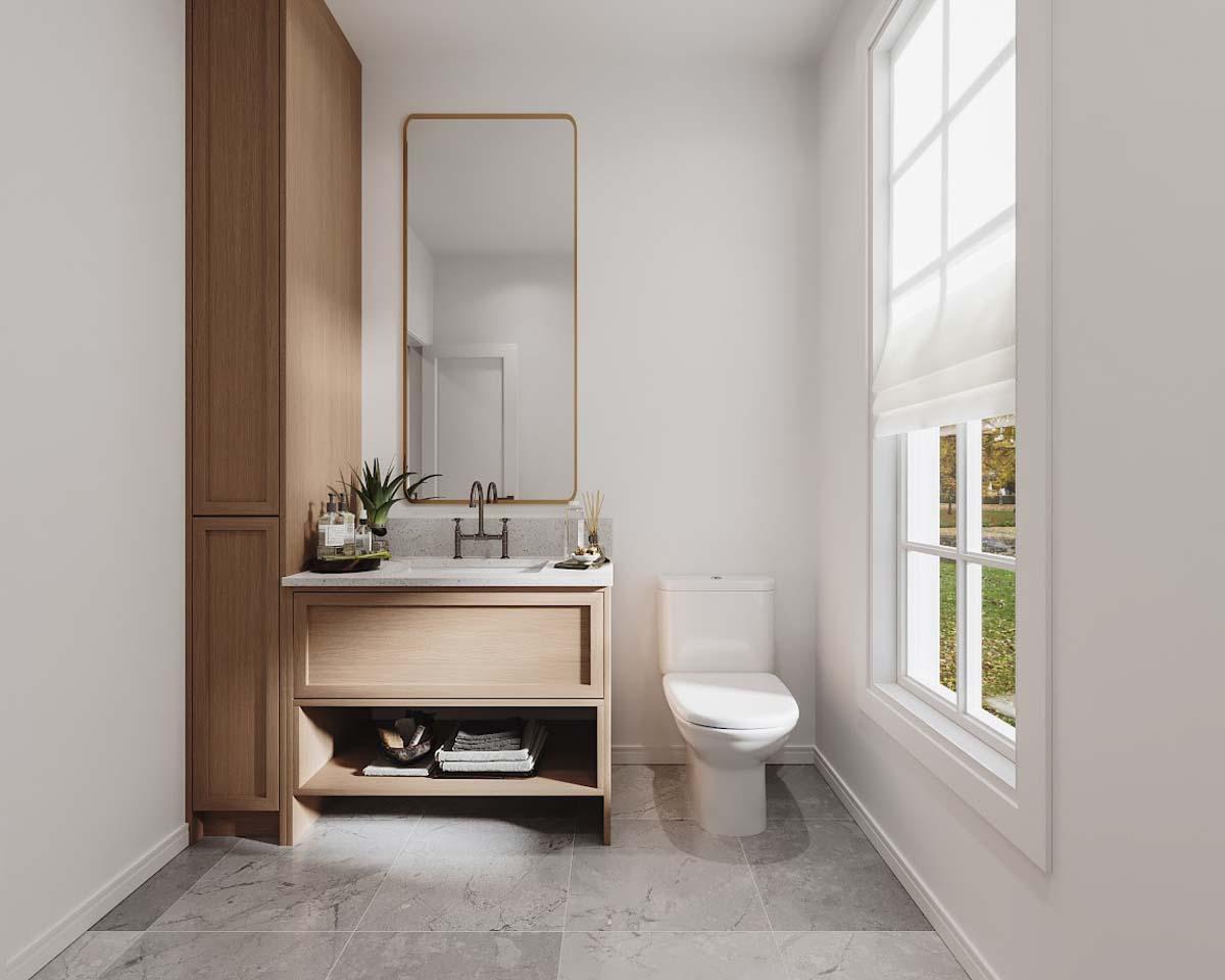 A modern bathroom features a vanity with a large mirror, a toilet, and a window with a view of greenery. Natural light fills the space.