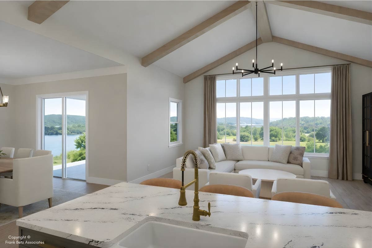 Interior view of great room with vaulted ceiling, exposed beams, large window, and sectional sofa. Open to dining area with lake view.