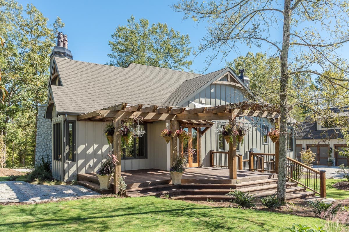 House plan exterior: Modern Farmhouse style, one story, with a stone chimney, gables, and a wooden pergola over a deck.