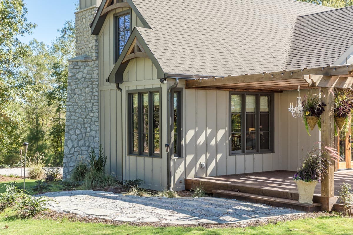 House plan exterior shows stone chimney, board and batten siding, dormer with wood accents, and wood pergola.