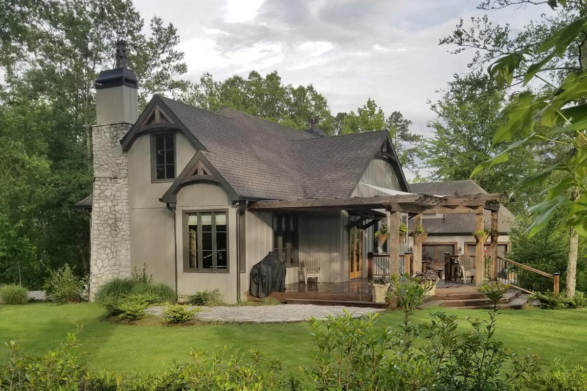 House plan exterior with stone chimney, prominent gables, and wooden pergola over deck.