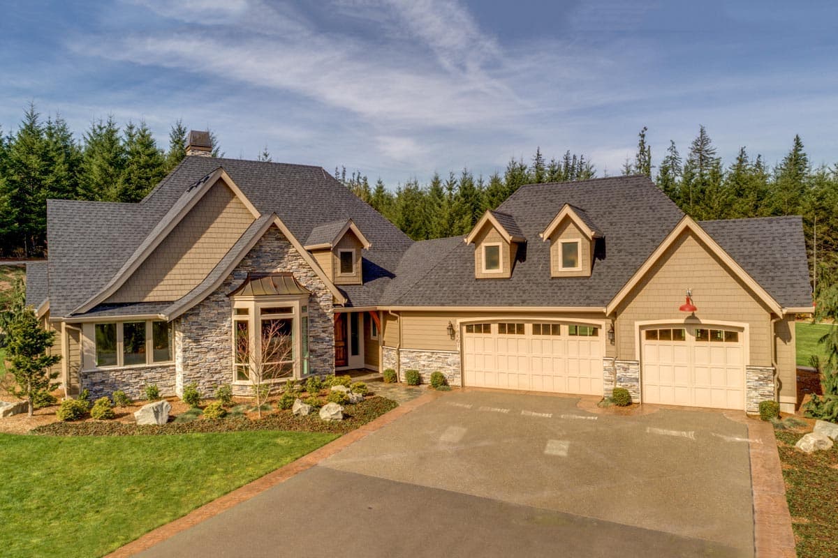 House plan exterior: Two-story home with stone and shingle siding, multiple gables, dormers, and a three-car garage.