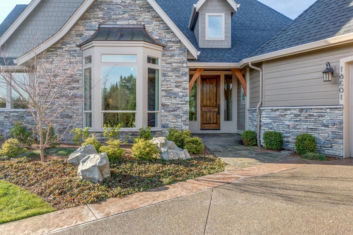House plan exterior with stone facade, bay window, gabled dormer, and arched wooden entry.