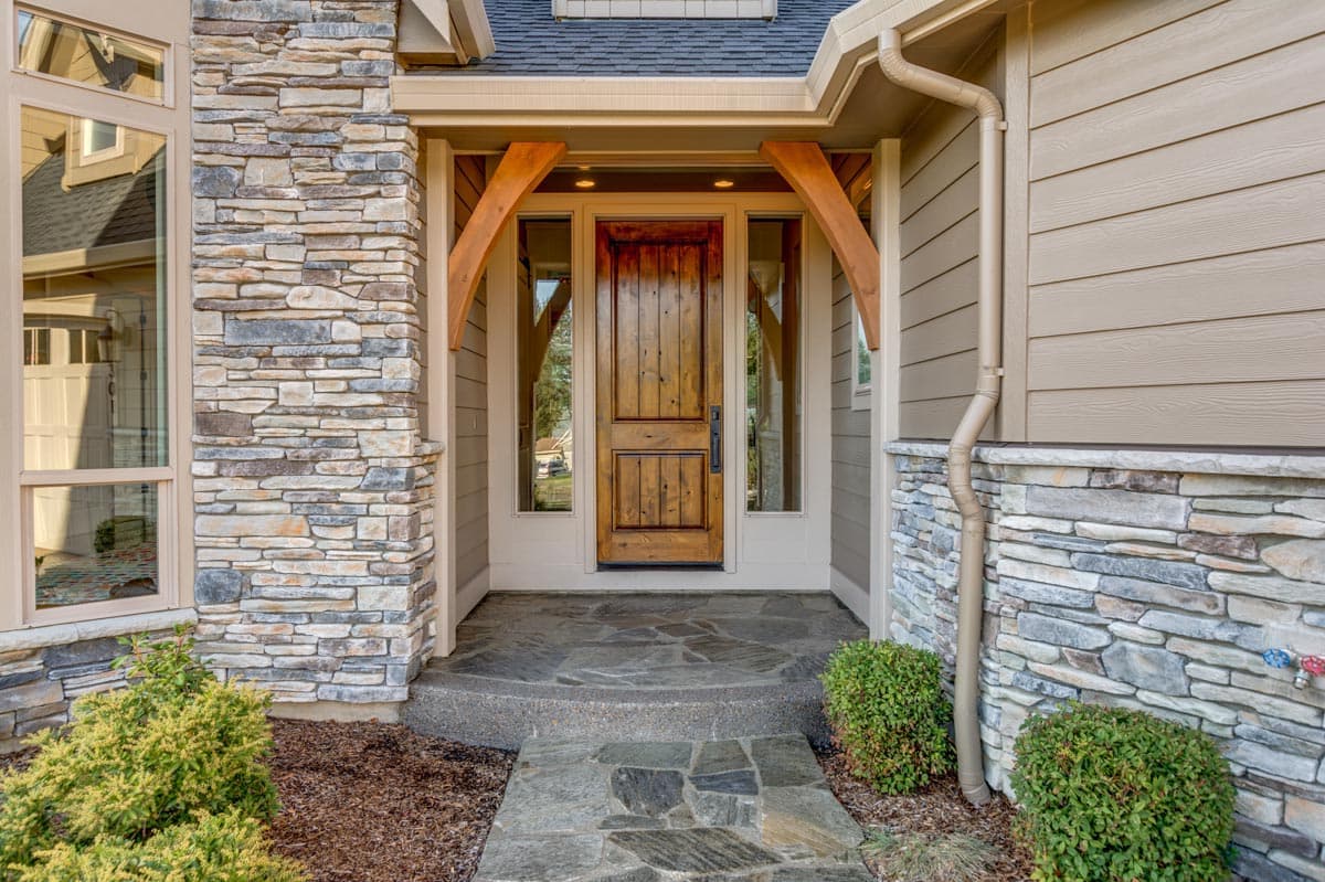 House plan exterior showing a covered entryway with stone accents, wooden door, and arched support beams.