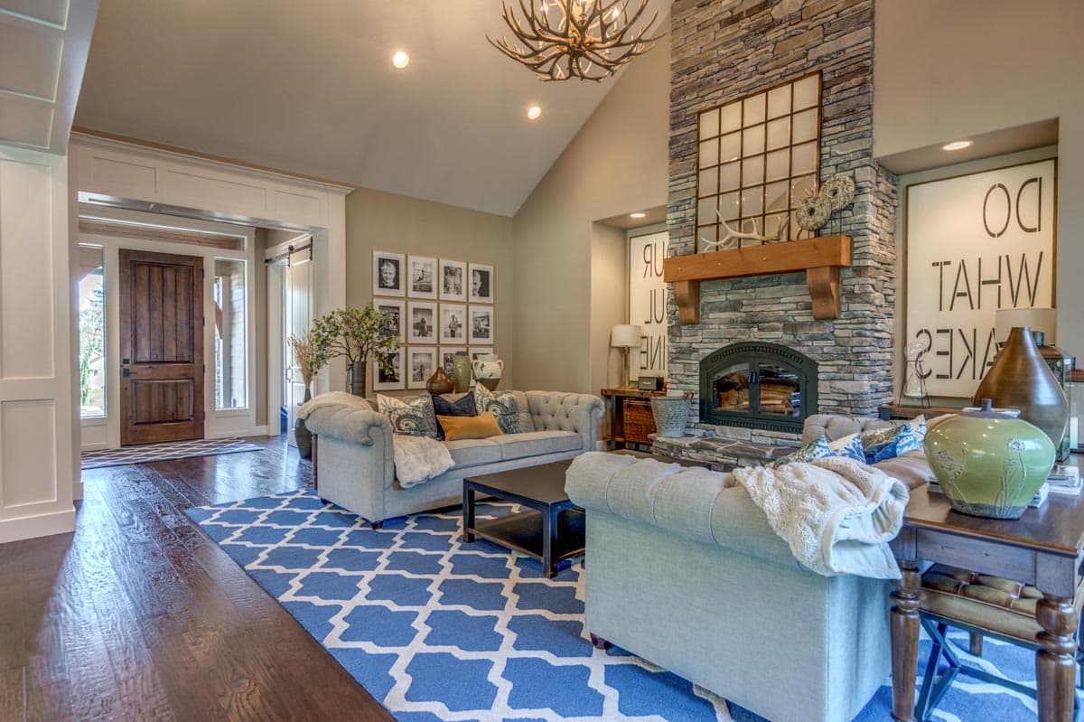 Living room with vaulted ceiling, stone fireplace with wood mantel, and large double doors to entryway.