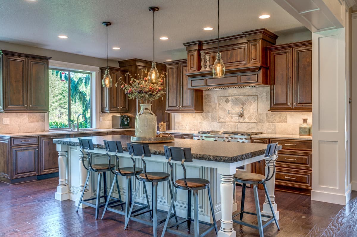 Kitchen featuring a large island with seating, dark wood cabinetry, decorative range hood, and a large window overlooking trees.