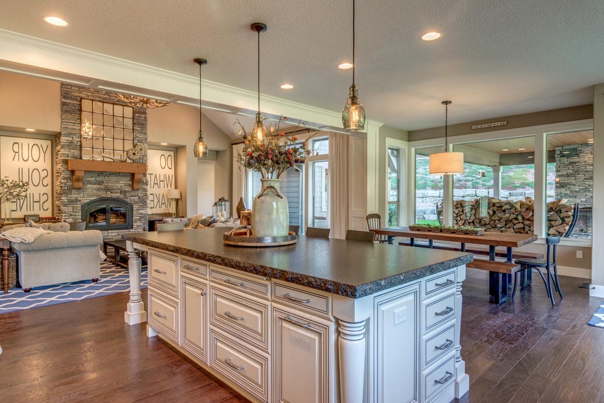 Open-concept kitchen and great room with stone fireplace, large island with seating, and dining area with view of outdoor space.