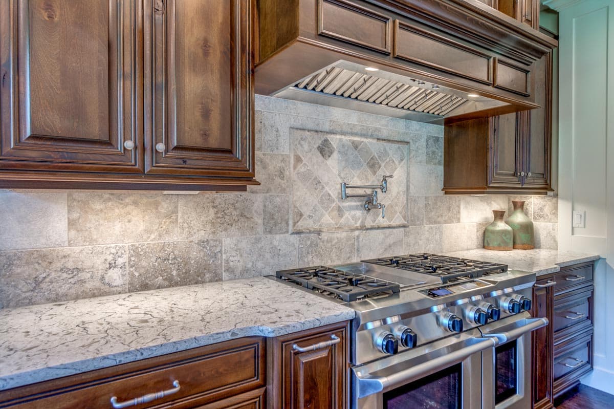Kitchen with dark wood cabinets, granite counters, stainless steel range, pot filler, and stone tile backsplash.
