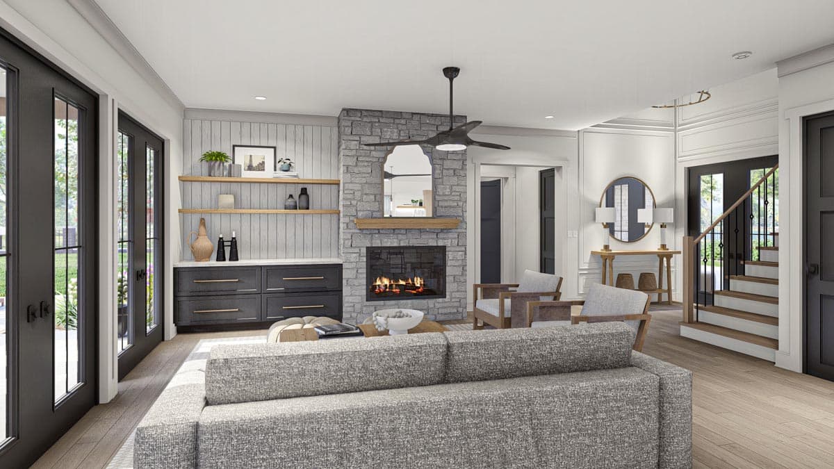 Living room with stone fireplace, built-in cabinetry, gray sectional sofa, and stairs to second floor.