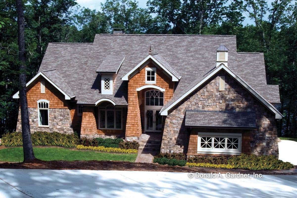 House plan exterior: stone and wood siding, multiple gables, dormer with decorative grille, arched entrance.