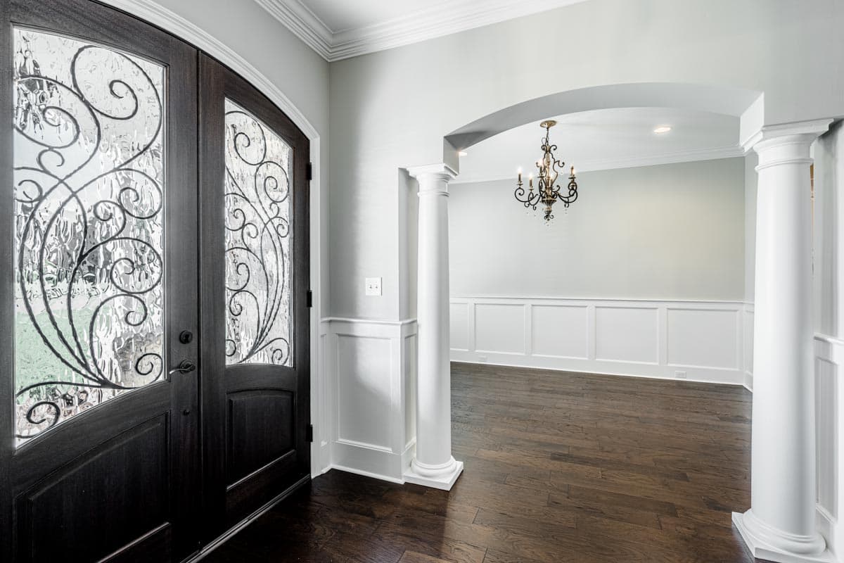 Entryway with arched opening, decorative double doors, wainscoting, and a chandelier.