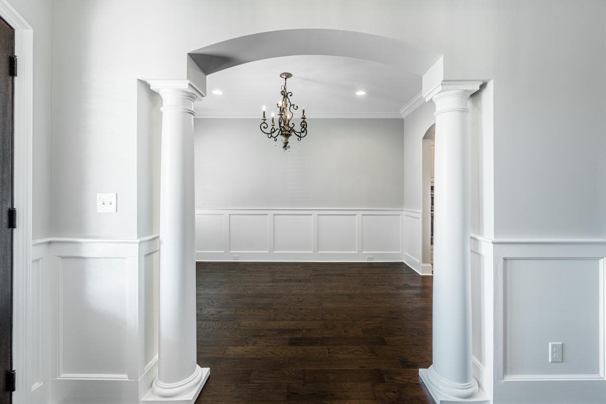 Interior view shows an arched entryway with classical columns framing a dining room with wainscoting and dark wood floors.