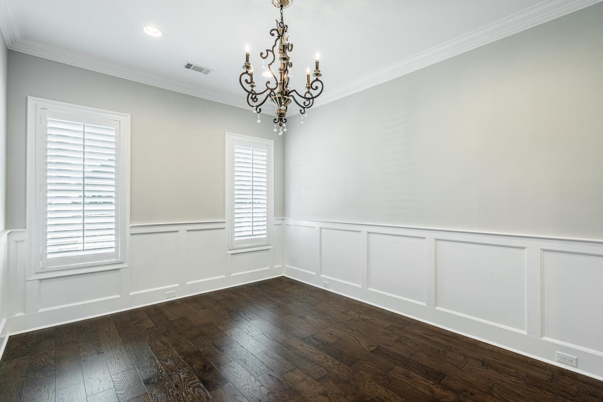 Interior view of a room with dark hardwood floors, plantation shutters on windows, and decorative wall paneling.