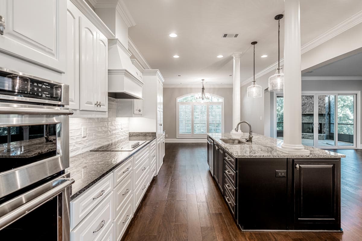 Kitchen with white cabinetry, granite countertops, large island with sink, and stainless steel appliances. Arched window and fireplace visible.