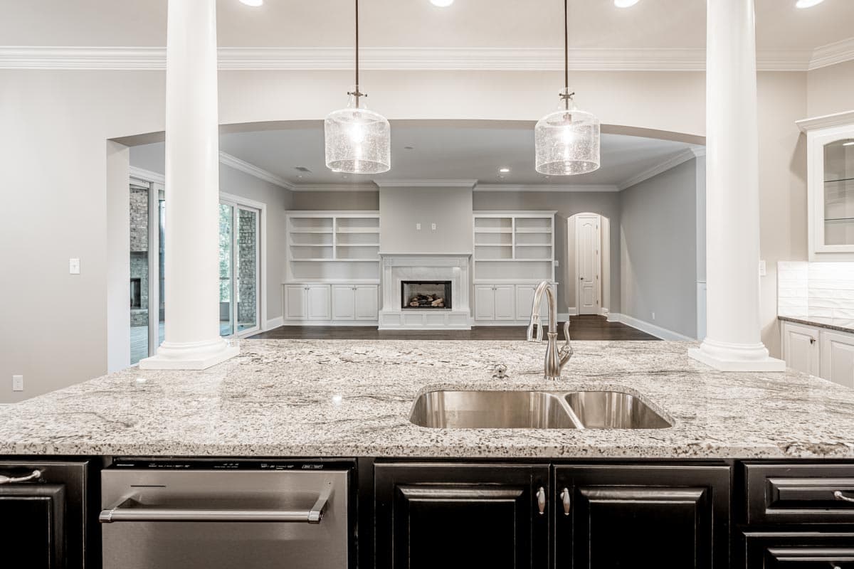 Kitchen island with sink and dishwasher opens to great room with fireplace and built-in shelving.