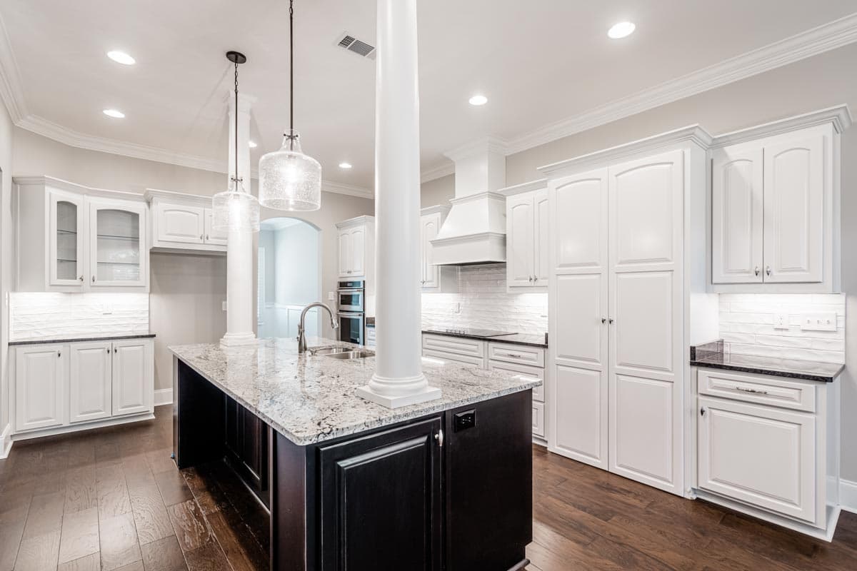 Kitchen interior with central island, white cabinetry, subway tile backsplash, and stainless steel appliances.