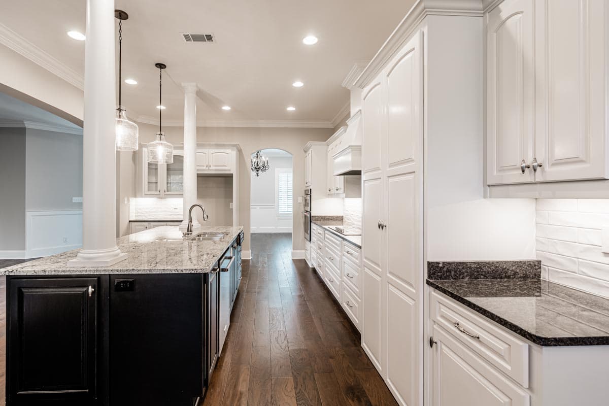 Kitchen with granite island, white cabinetry, pendant lights, and dark hardwood floors.