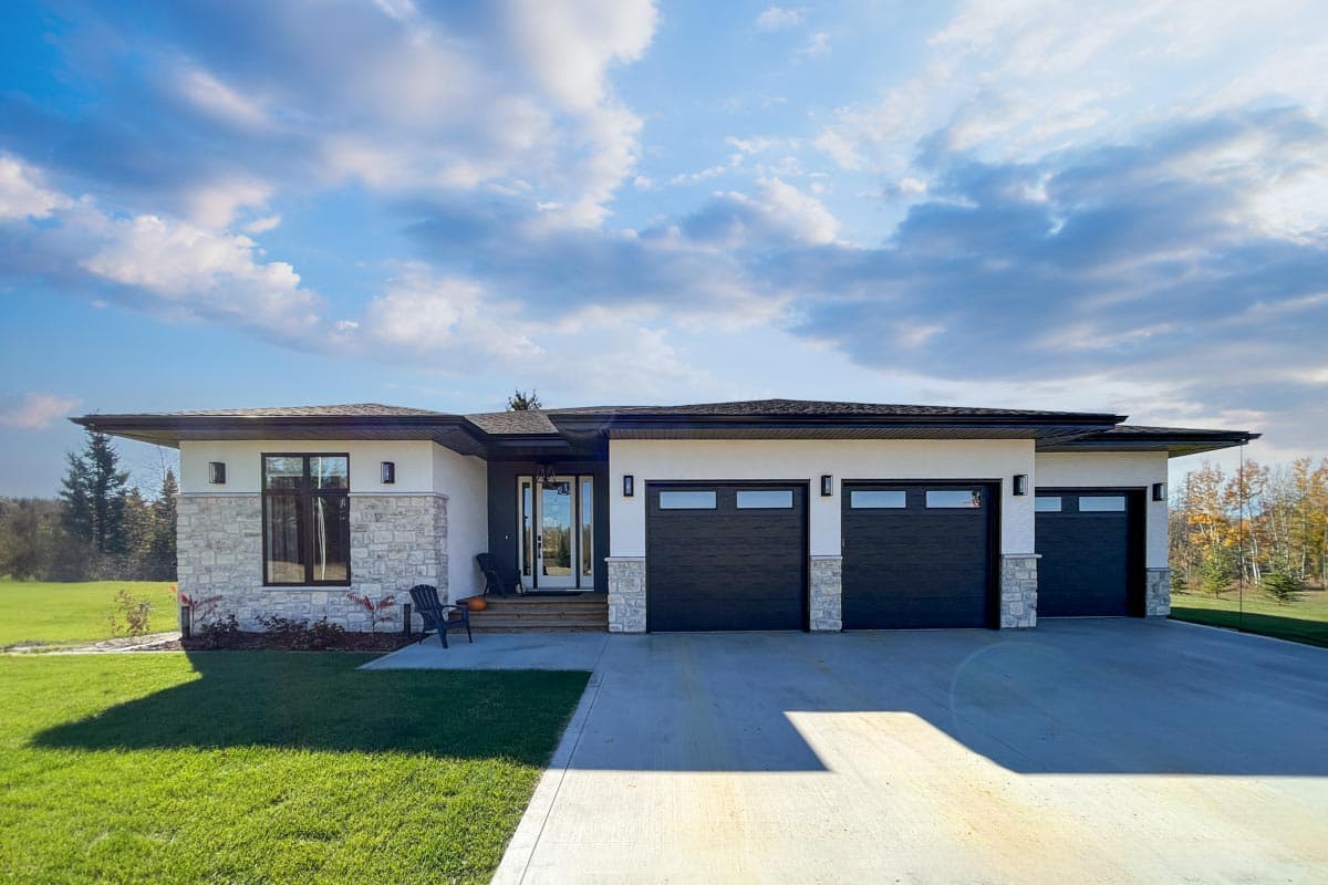 House plan exterior. Modern, one-story home with a flat roof, stone accents, and a three-car garage. Features include large windows and a covered entrance.