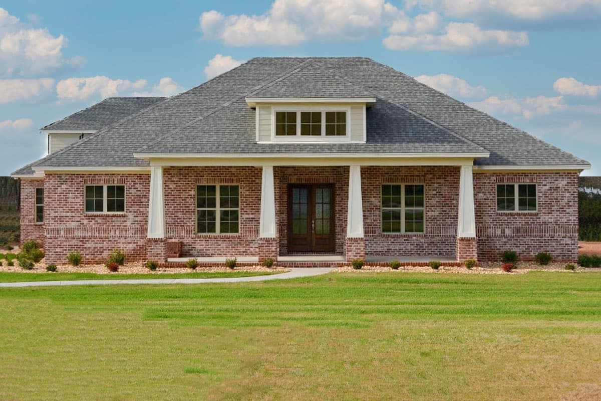 House plan exterior. Two-story brick home with a gable roof, covered porch supported by columns, and dormer with multiple windows.