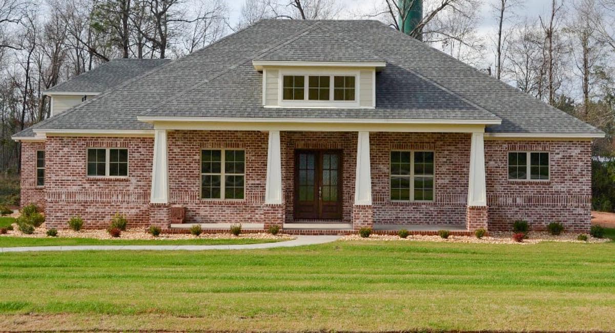 House plan exterior: Traditional brick home with a prominent covered front porch, double entry doors, and a dormer above.