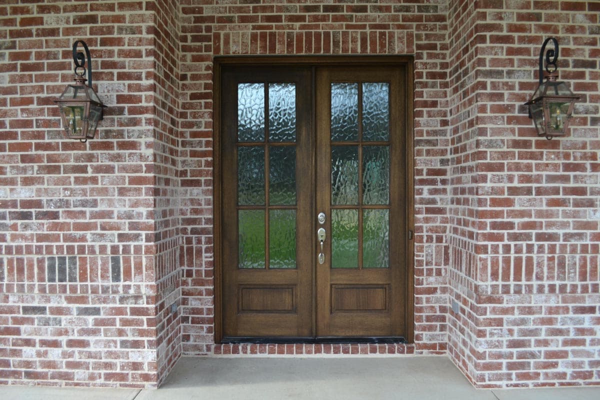 Exterior view of house plan: brick facade with double wooden doors with glass panes and two hanging lanterns.