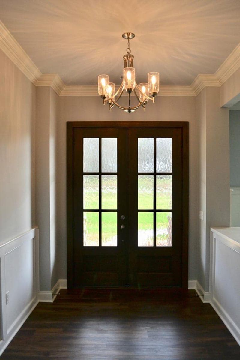 Interior view of double entry doors with glass panes and a five-light chandelier above.