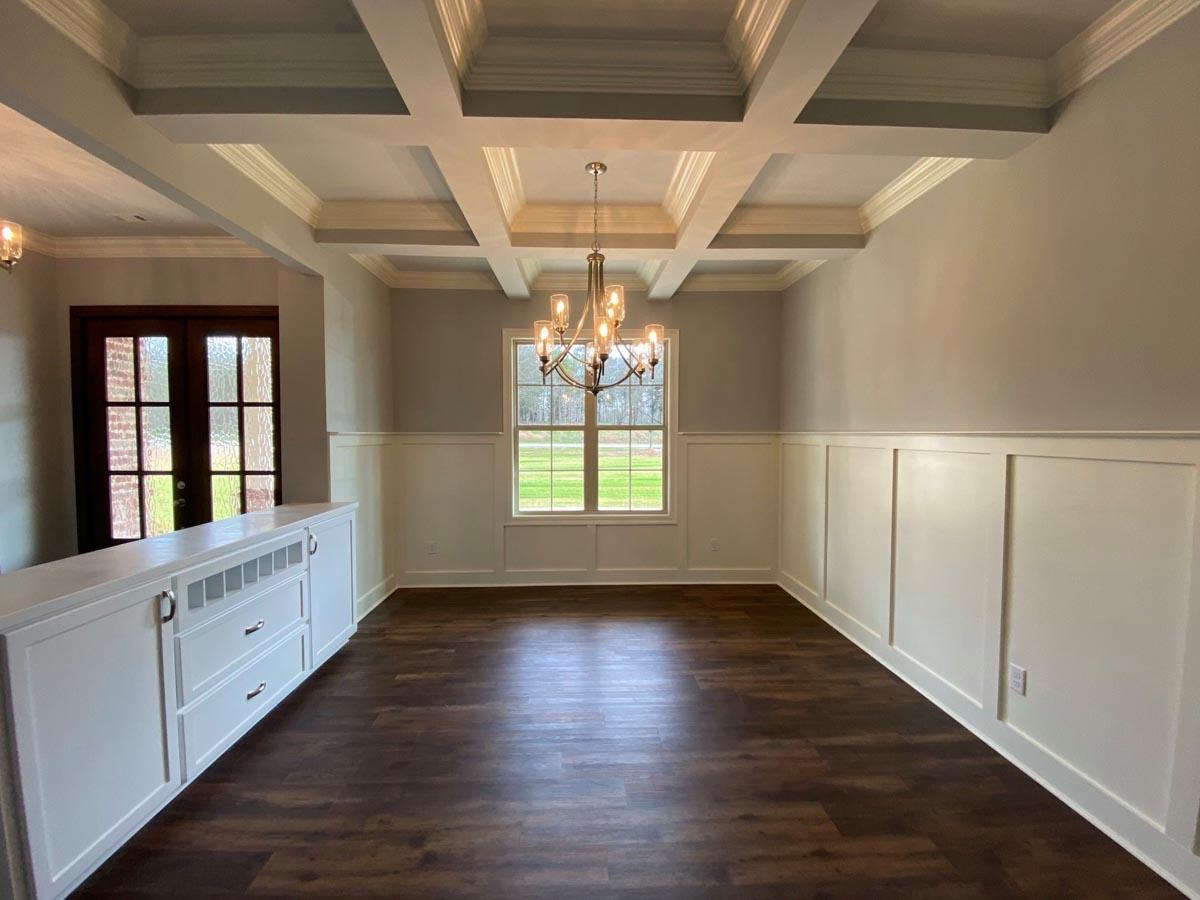 Interior view of a dining room with coffered ceiling, wainscoting, built-in cabinetry, and a large window.