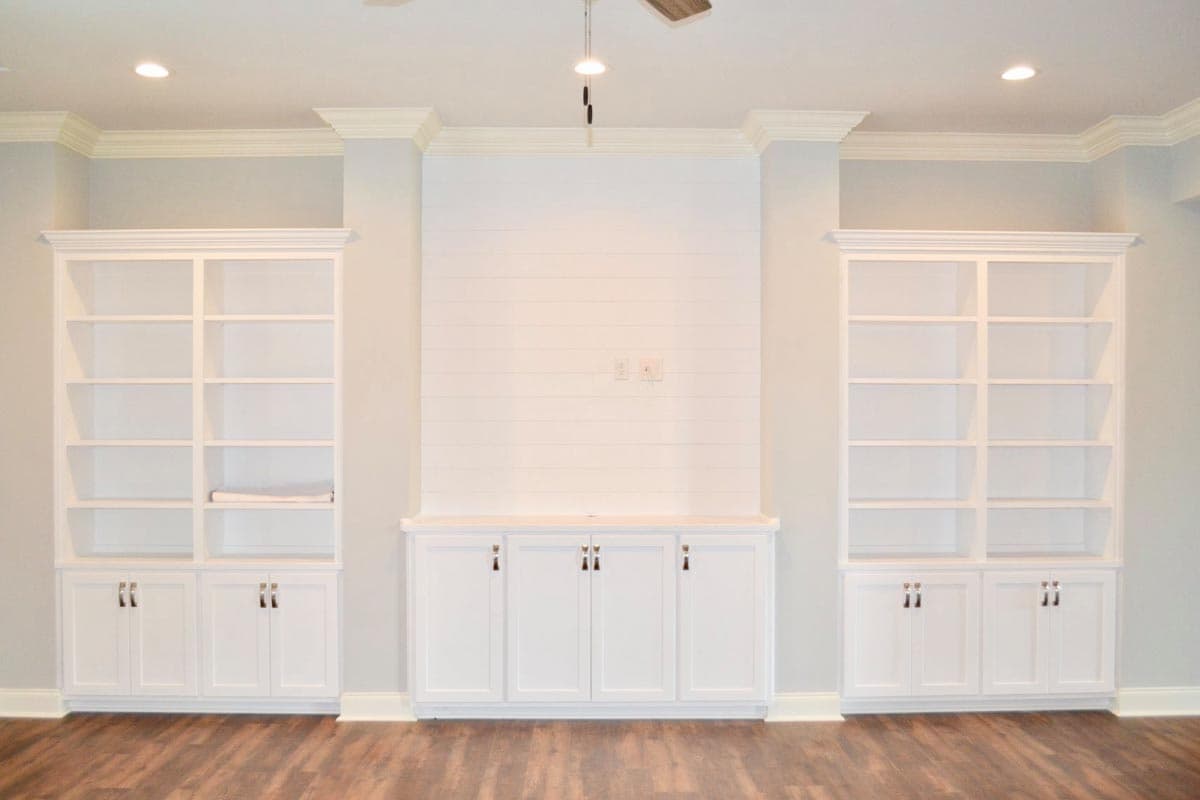 Built-in white shelving units flank a shiplap-clad entertainment center with lower cabinets.