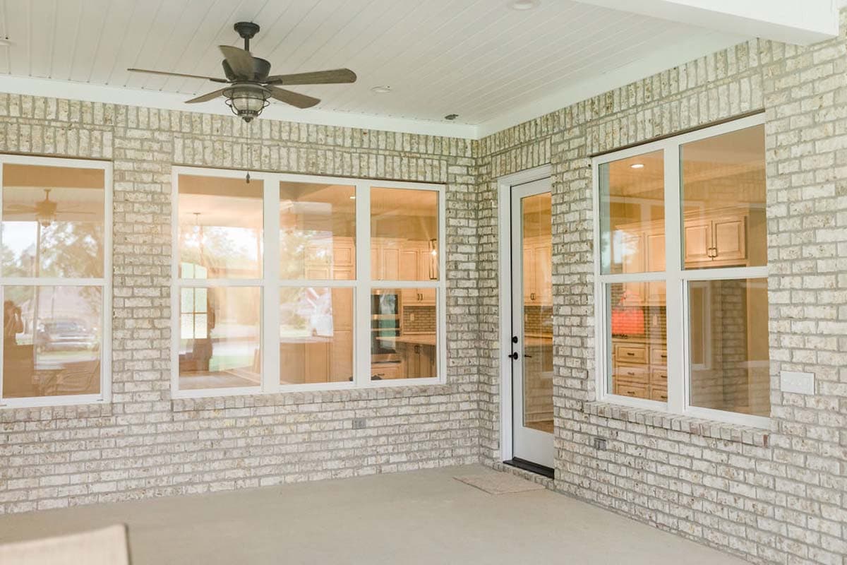 Covered porch with white-framed windows and a door revealing a kitchen with wood cabinets and a brick backsplash.