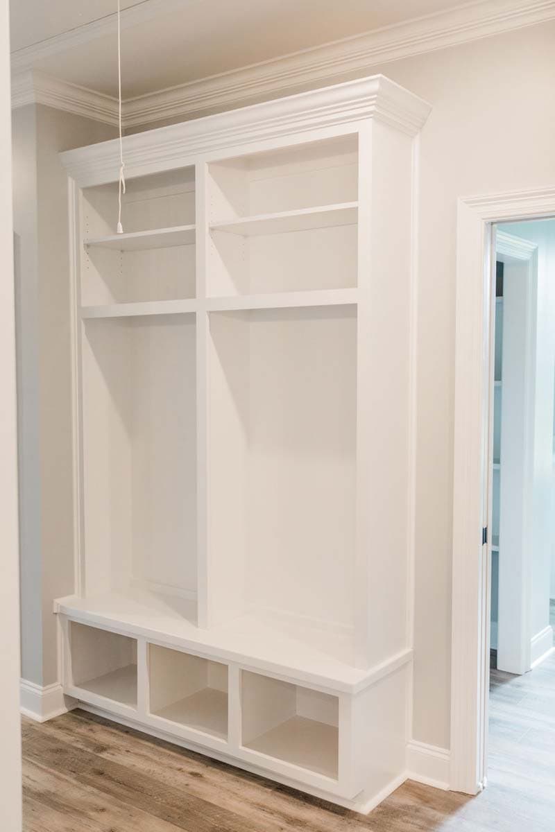 Built-in white shelving unit with bench seat, open cubbies, and crown molding.