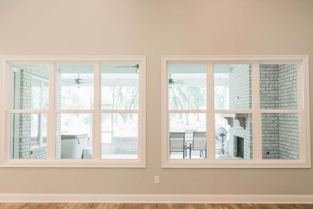 Interior view shows two large windows. Left window reveals screened porch with hot tub. Right window shows brick fireplace and outdoor seating.